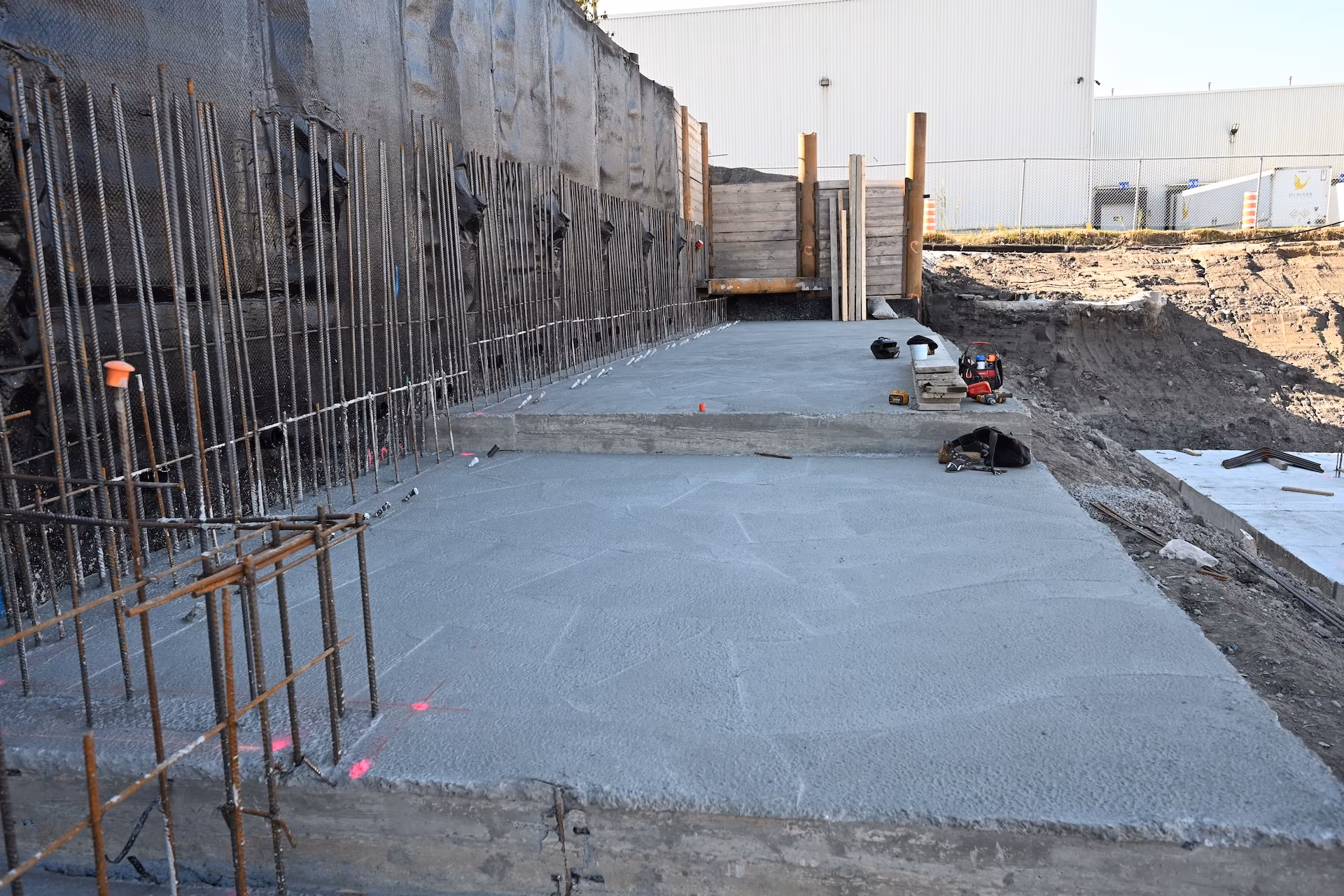 Concrete slab foundation under construction with exposed rebar and wooden supports at a building site.